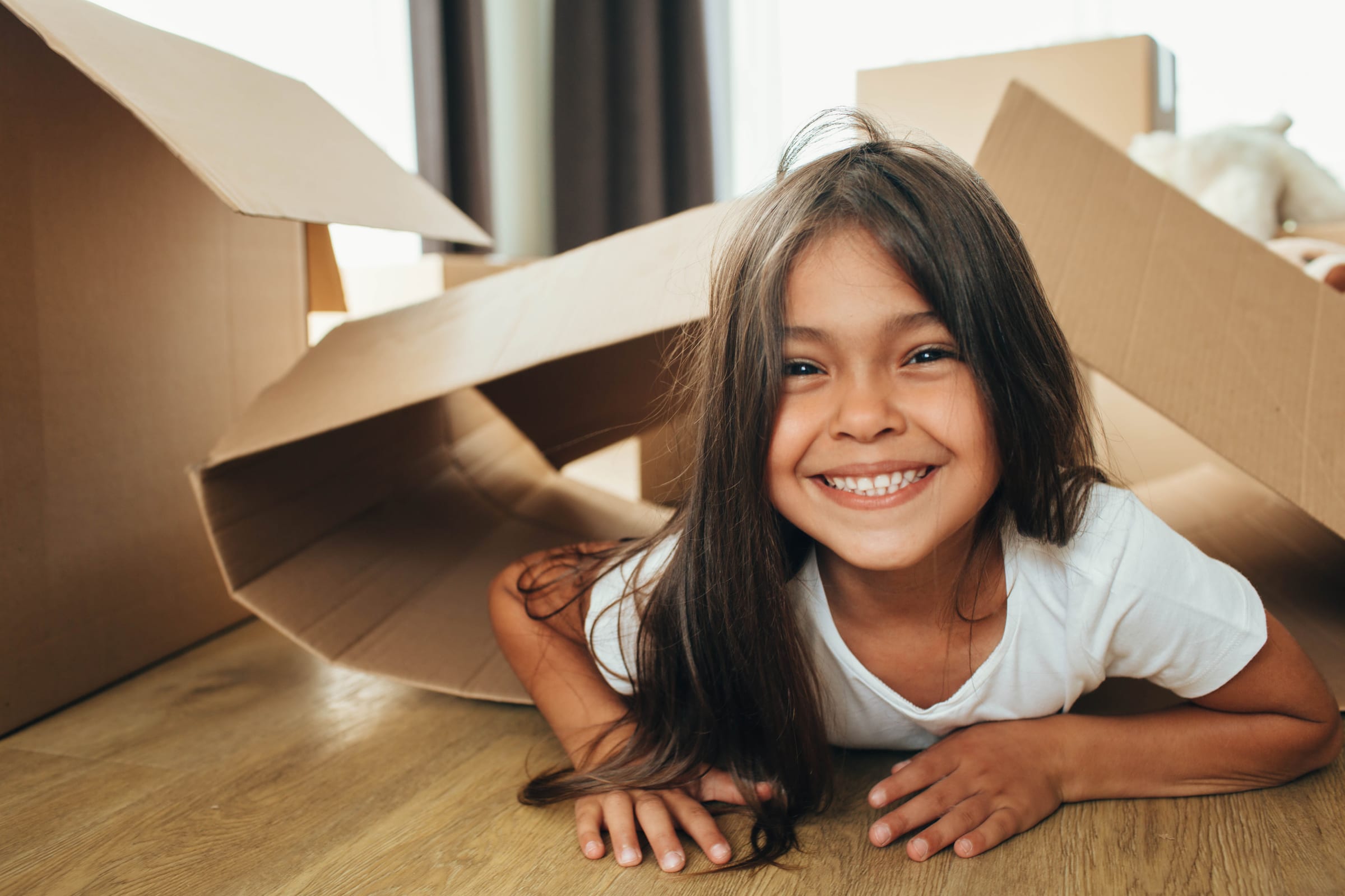 Smiling girl playing under a cardboard box fort